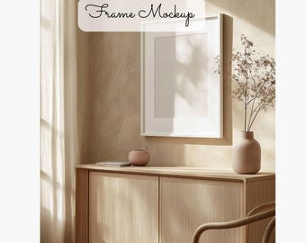 Può includere: Un mockup di cornice bianca appeso a una parete beige sopra un mobile in legno chiaro con due ante. Un piccolo vaso in terracotta con fiori secchi si trova sul mobile. Il testo "Frame Mockup" è scritto in corsivo sopra la cornice.