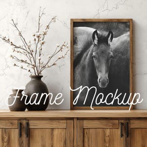 May include: A framed black and white photograph of a horse's head. The frame is made of wood. The image is displayed on a wooden cabinet with a vase and decorative branches. The text "Frame Mockup" is written in cursive.