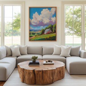 May include: A living room with a large, light gray sectional sofa, white pillows, and a round wooden coffee table. A framed landscape painting of a farm scene hangs above the sofa. Large windows offer a view of the outdoors.