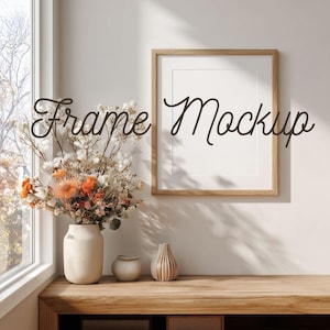 May include: A wooden framed art print mockup with the text "Frame Mockup" in a cursive font. A vase of dried flowers and two decorative vases sit on a wooden table. A window is visible in the background.