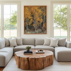 May include: A living room featuring a large, light gray sectional sofa with white throw pillows. A large, round wooden coffee table sits on a light-colored rug. A framed landscape photograph of autumn trees hangs above the sofa.