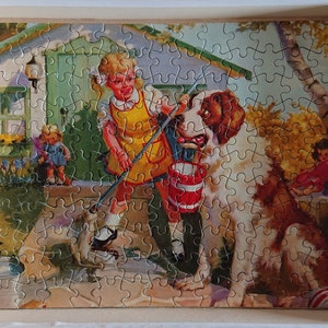May include: A vintage jigsaw puzzle showing a girl in a yellow dress and a St. Bernard dog holding a bucket. The puzzle is set in a garden with a house in the background.
