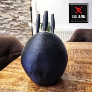 May include: Black ceramic Totoro figurine with three long ears. The figurine is sitting on a wooden table.