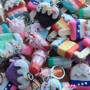 May include: A collection of colorful, handmade polymer clay charms shaped like ice cream, milkshakes, and popsicles. Each charm features a unique design and is attached to a silver key ring.