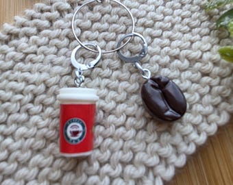 May include: A set of two knitting stitch markers featuring a coffee cup and a coffee bean. The markers are attached to a silver ring.
