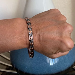 May include: A copper and black magnetic bracelet with a cross design.