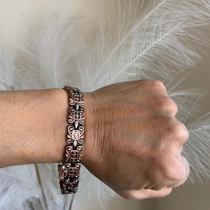 Peut inclure: Un bracelet en cuivre avec un design orné et détaillé. Le bracelet est composé de pièces métalliques reliées entre elles avec un motif en forme de croix.