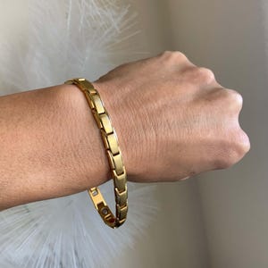 May include: A gold-toned magnetic bracelet with a chain-link design. The bracelet is worn on a person's wrist.