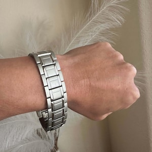 Peut inclure: Un bracelet de montre en métal argenté avec une finition polie. Le bracelet est composé de maillons individuels qui sont reliés entre eux.
