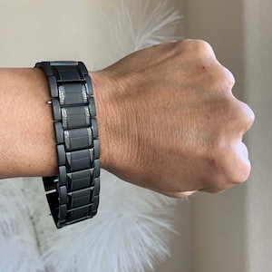 May include: A black metal watch band with a brushed finish. The band has a clasp closure and is designed for a wrist watch.