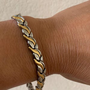 Könnte beinhalten: Ein magnetisches Armband aus Silber und Gold mit geflochtenem Design.