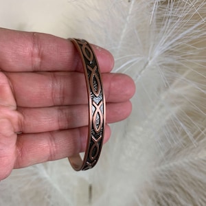 May include: A copper bracelet with a repeating pattern of the Ichthys symbol, a Christian symbol representing Jesus Christ.