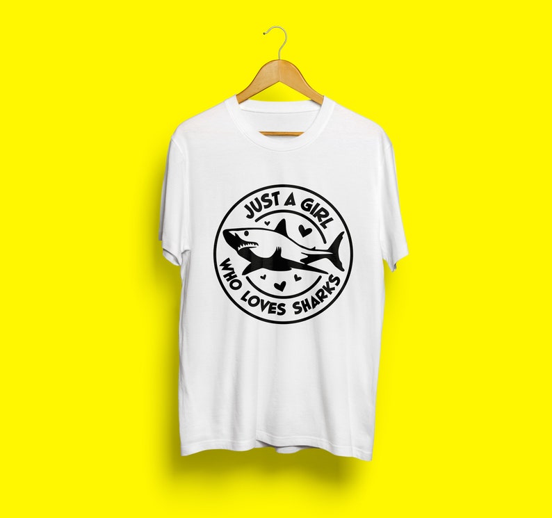 May include: White t-shirt with a black circle graphic featuring a shark and the text "Just a girl who loves sharks".