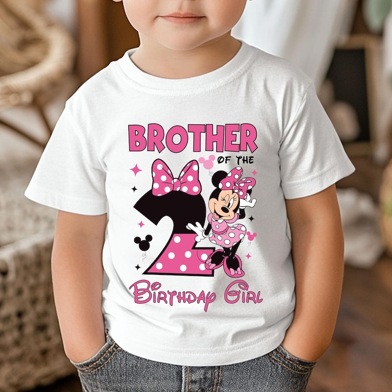 Puede incluir: Camiseta blanca con un dise&ntilde;o de Minnie Mouse rosa y negro. La camiseta presenta el texto "BROTHER of the BIRTHAY GIRL" y un gran n&uacute;mero "2" con lunares rosas. Minnie Mouse lleva un vestido de lunares rosas.