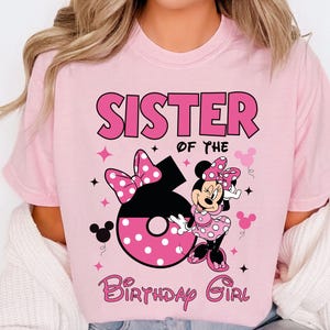 May include: Pink t-shirt with the text "SISTER OF THE BIRTHDAY GIRL". The shirt features a graphic of Minnie Mouse, a large number 6, and polka dot bows. The design is in shades of pink and black.