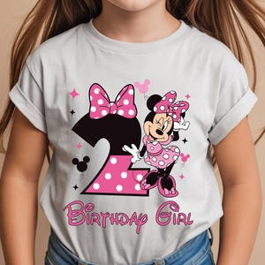 Puede incluir: Camiseta gris claro con un gr&aacute;fico de Minnie Mouse. El dise&ntilde;o incluye un gran n&uacute;mero 2 rosa con lunares blancos, un lazo rosa y las palabras "Birthday Girl" en escritura rosa.