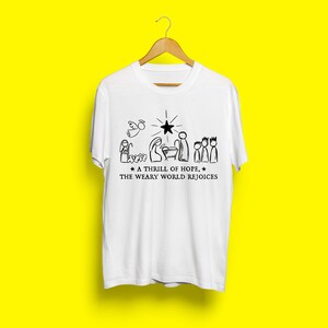 May include: White t-shirt with a black and white illustration of the nativity scene. The text reads "A thrill of hope, the weary world rejoices."