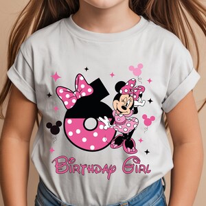 May include: A light gray t-shirt featuring a Minnie Mouse graphic. The design includes a large number 6 with pink polka dots, a bow, and the words "Birthday Girl" in pink script. Minnie Mouse is also featured.