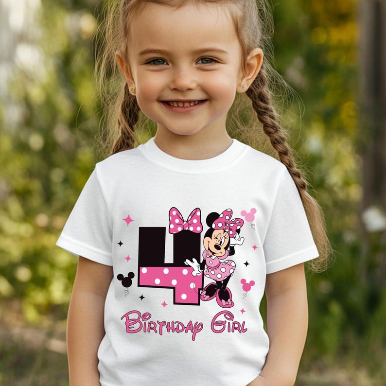 May include: White t-shirt with a Minnie Mouse graphic, a pink polka dot "4", and the words "Birthday Girl". The design includes pink bows and stars. The shirt is for a child.