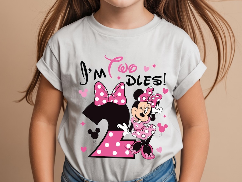 May include: A light gray t-shirt featuring a graphic of Minnie Mouse and the text "I'm Two Dles!" in pink and black. The number 2 is pink with white polka dots. Hearts and stars are also included.