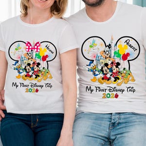 May include: White t-shirts with a Disney theme. Each shirt features a Mickey Mouse ear design with Disney characters, balloons, and the text "My First Disney Trip 2020." One shirt has "Helena" and the other "Albert".