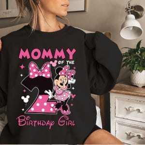 Puede incluir: Sudadera negra con un dise&ntilde;o de Minnie Mouse rosa. El dise&ntilde;o incluye el texto "MOMMY OF THE BIRTHDAY GIRL" y un gran n&uacute;mero "2" con lunares. Minnie Mouse lleva un vestido rosa con lunares.