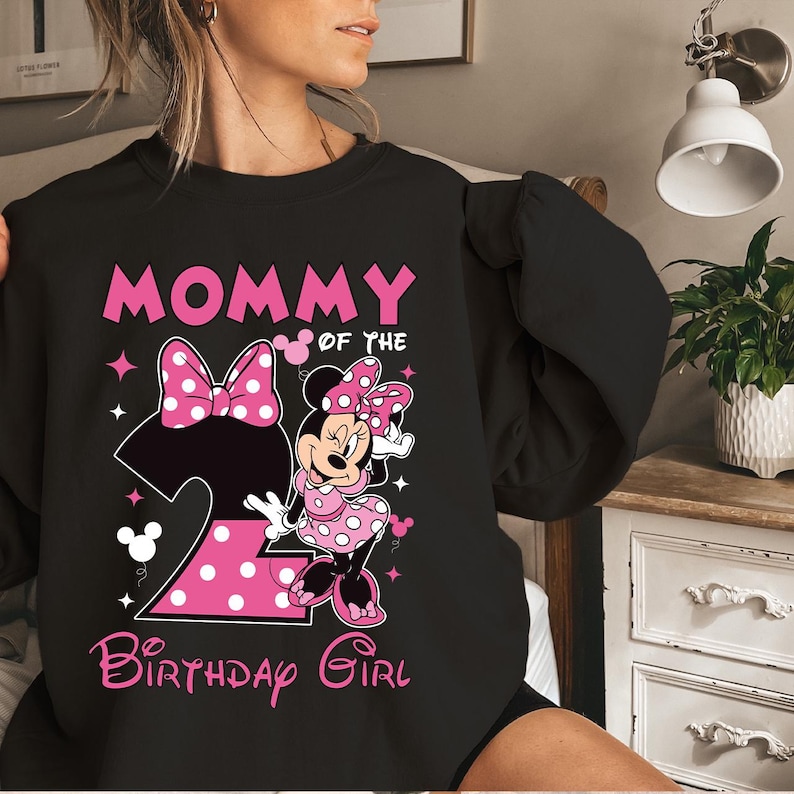 Puede incluir: Sudadera negra con un dise&ntilde;o de Minnie Mouse rosa. El dise&ntilde;o incluye el texto "MOMMY OF THE BIRTHDAY GIRL" y un gran n&uacute;mero "2" con lunares. Minnie Mouse lleva un vestido rosa con lunares.