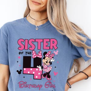 May include: A blue t-shirt featuring the text "SISTER of the 4 Birthday Girl" in pink. The design includes a Minnie Mouse graphic with a polka dot bow and dress. The number 4 is also in pink polka dots.