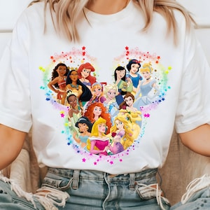 May include: White t-shirt featuring a colorful graphic of Disney princesses arranged in a heart shape. The design includes characters like Ariel, Belle, and Elsa, surrounded by stars and a rainbow gradient.