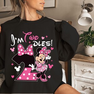 May include: Black sweatshirt featuring Minnie Mouse with the text "I'm Two Dles!" in white and pink. The design includes a large pink polka dot bow, the number 2, and Minnie Mouse in a pink polka dot dress.