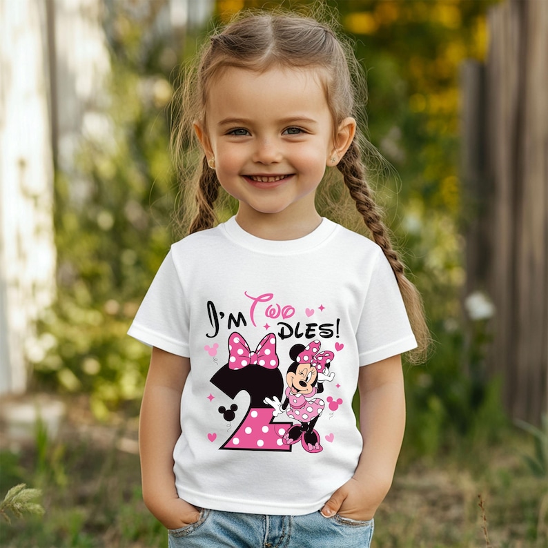 May include: A white t-shirt with the text "I'm Two Dles!" in pink and black, featuring a Minnie Mouse graphic. The number "2" is in pink with white polka dots. The shirt is worn by a young girl.