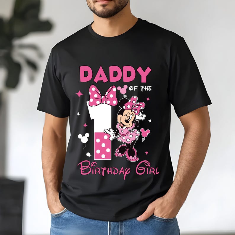 May include: Black t-shirt with a pink graphic featuring the text "DADDY of the BIRTHDAY GIRL" and a Minnie Mouse design. The number 1 is also in pink with white polka dots. The shirt has short sleeves and a crew neck.