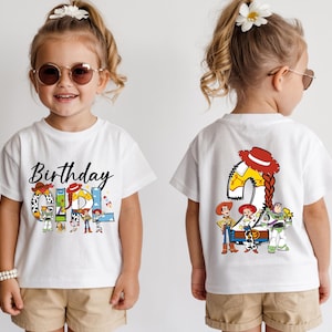 May include: White t-shirt with a colorful "Birthday Girl" graphic featuring characters from the Toy Story movie. The back of the shirt displays a large number "2" with the same characters. The shirt is worn by a young child.