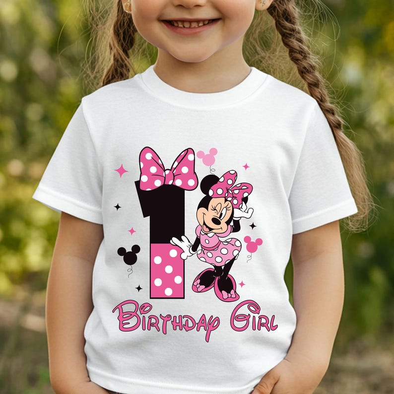 May include: White t-shirt featuring a Minnie Mouse graphic with a pink polka dot bow and dress. The number 1 is in black with pink polka dots. The words "Birthday Girl" are in pink script.