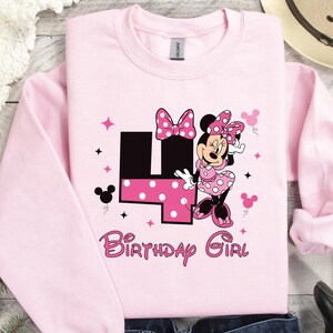 May include: Pale pink sweatshirt with a Minnie Mouse design. The graphic includes a large number 4 with polka dots, Minnie Mouse, and the words "Birthday Girl" in pink. The sweatshirt has long sleeves and a crew neck.