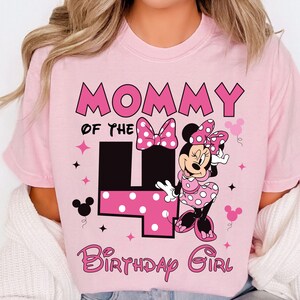 May include: A pink t-shirt with the text "Mommy of the 4 Birthday Girl" in pink and black. It features a Minnie Mouse graphic in a polka dot dress and bow. Includes star and Mickey Mouse head accents.