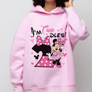 May include: A light pink hooded sweatshirt featuring a Minnie Mouse graphic. The design includes the text "I'm Two DLES!" with a large number 2, a polka dot bow, and Minnie Mouse. The sweatshirt is a comfortable, casual style.
