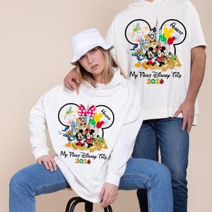May include: White sweatshirts with Disney characters and the text "My First Disney Trip 2026". One sweatshirt features a Minnie Mouse bow and the name "Helena", the other has Mickey Mouse ears and the name "Albert".