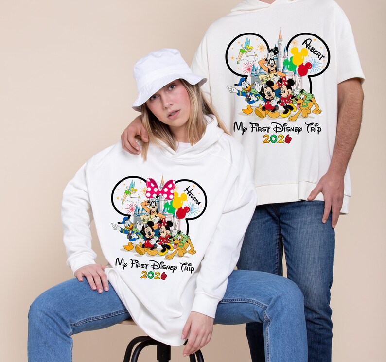May include: White sweatshirts with Disney characters and the text "My First Disney Trip 2026". One sweatshirt features a Minnie Mouse bow and the name "Helena", the other has Mickey Mouse ears and the name "Albert".