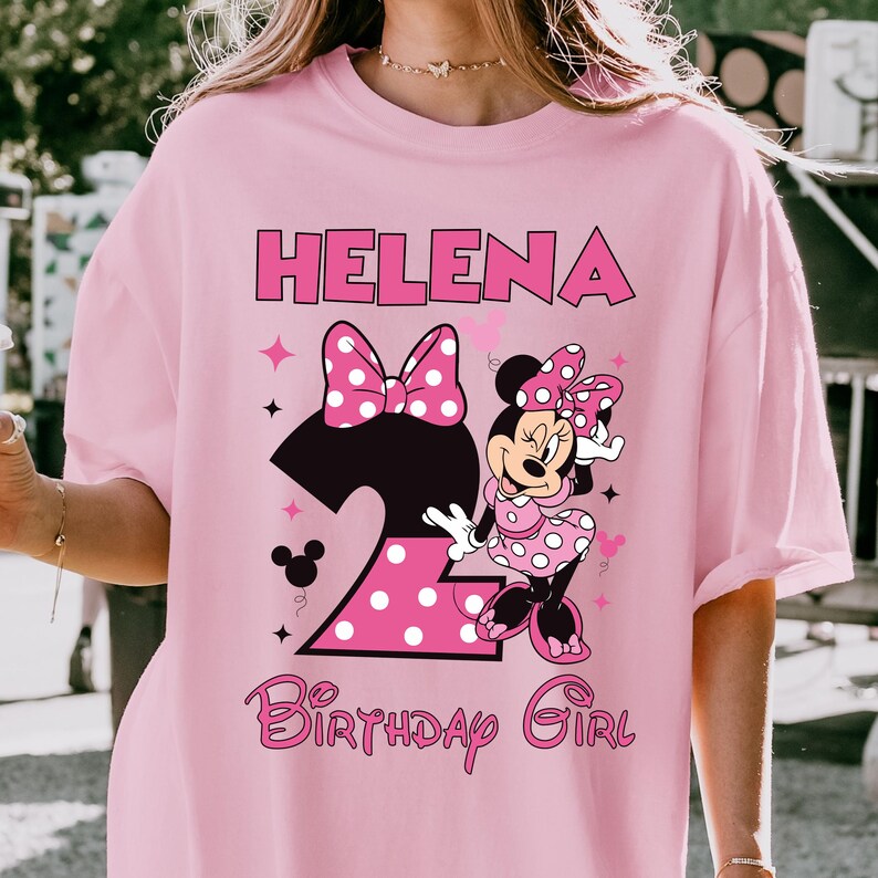 Puede incluir: Camiseta rosa con el nombre "Helena" en letras rosas. El n&uacute;mero "2" es negro con un lazo rosa de lunares. Minnie Mouse lleva un vestido rosa de lunares. El texto "Birthday Girl" est&aacute; en rosa.