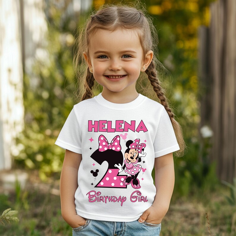 Puede incluir: Camiseta blanca con el nombre "Helena" en letras rosas. La camiseta presenta un gr&aacute;fico de Minnie Mouse con un lazo rosa de lunares y el n&uacute;mero "2" en lunares rosas. El texto "Birthday Girl" tambi&eacute;n est&aacute; impreso en la camiseta.