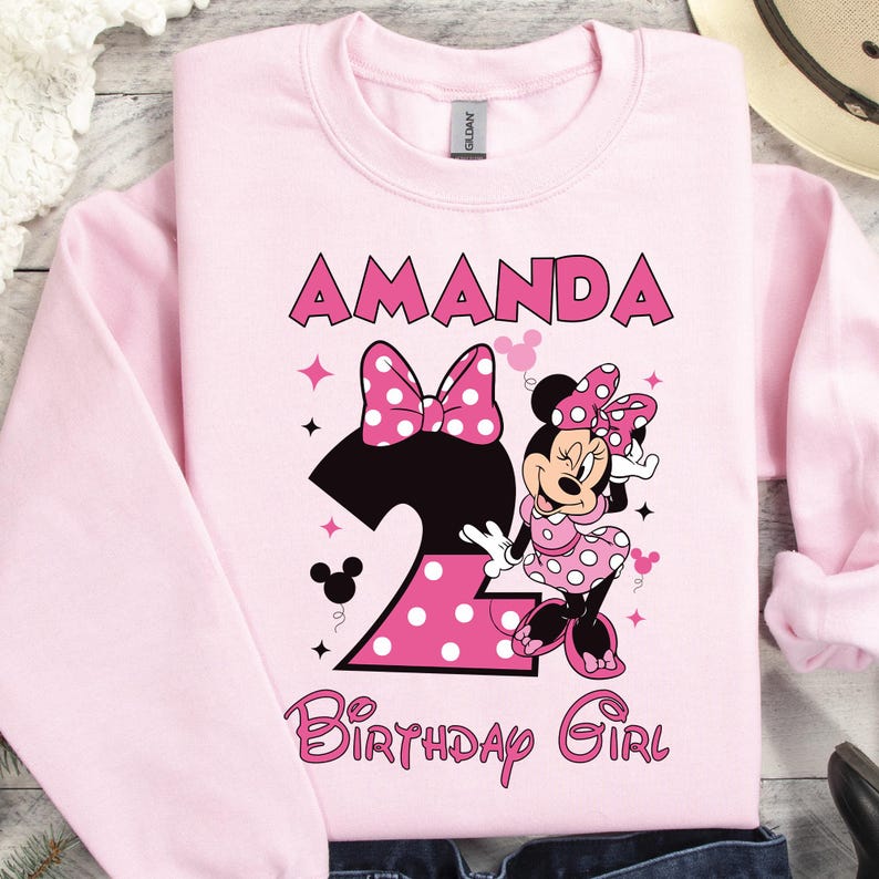 Puede incluir: Sudadera rosa claro con el nombre "AMANDA" en letras rosas. El n&uacute;mero "2" negro tiene lunares rosas. Minnie Mouse aparece a la derecha. Las palabras "Birthday Girl" est&aacute;n en rosa.