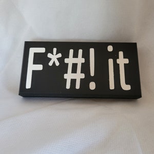 May include: Black wooden sign with white lettering that reads "F*#! it".