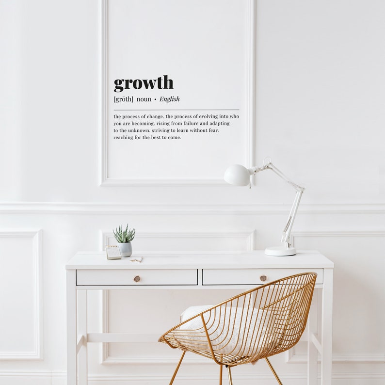 May include: A white desk with a gold wire chair and a lamp. The wall behind the desk has a black and white print with the word "growth" and its definition.