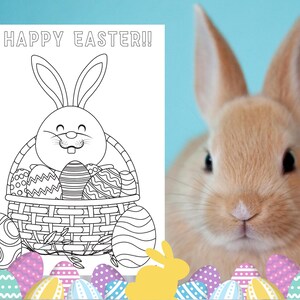 May include: A black and white coloring page featuring a bunny rabbit holding a basket full of Easter eggs. The text "HAPPY EASTER!" is at the top of the page. A real bunny rabbit is in the background.