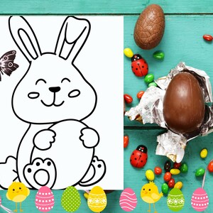 May include: A black and white line drawing of a bunny rabbit holding an egg. The bunny is smiling and has big eyes. The image is on a white sheet of paper with a blue wooden background. There are chocolate eggs, candy, and ladybugs scattered around the paper.