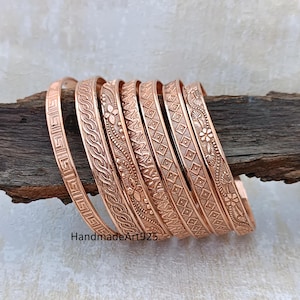 Peut inclure: Ensemble de bracelets de couleur cuivre avec des motifs en relief complexes, notamment floraux et géométriques. Les bracelets sont présentés sur un morceau de bois sombre. Le texte "HandmadeArt925" est visible.