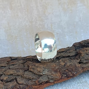 May include: A silver band ring with a rounded, smooth surface. The ring is sitting on a piece of wood.