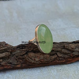 K&ouml;nnte beinhalten: Ein silberner Ring mit einem hellgr&uuml;nen ovalen Edelstein. Der Ring liegt auf einem St&uuml;ck Holz.