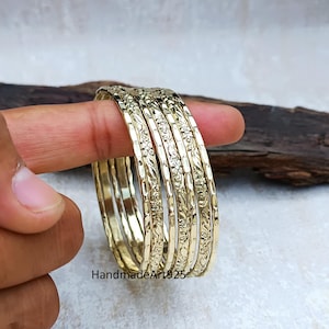 以下が含まれることがあります： 複雑な花の模様が施された、ゴールドトーンのバングル6個セット。バングルは重ねてあり、光沢のある仕上げになっています。